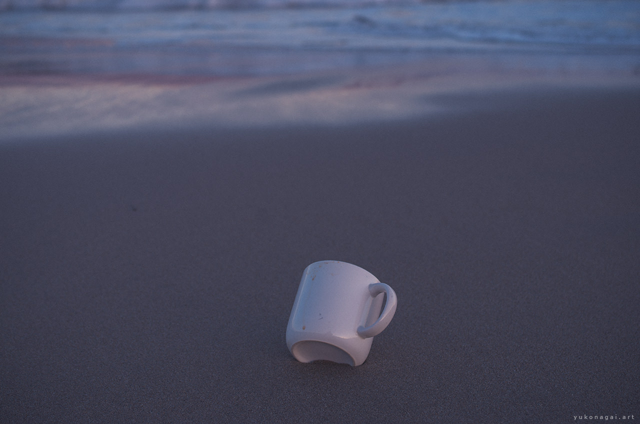 A large mug cup on sand at sea shore at sunset.